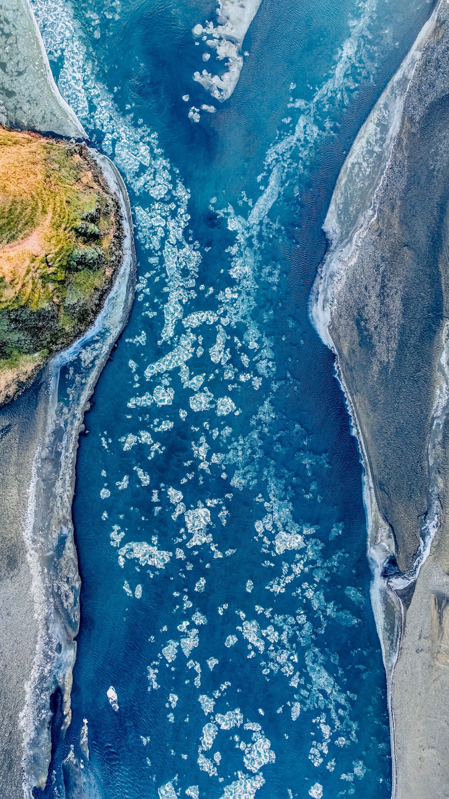 Chunks of ice drifting down a blue glacial river, seen from directly above