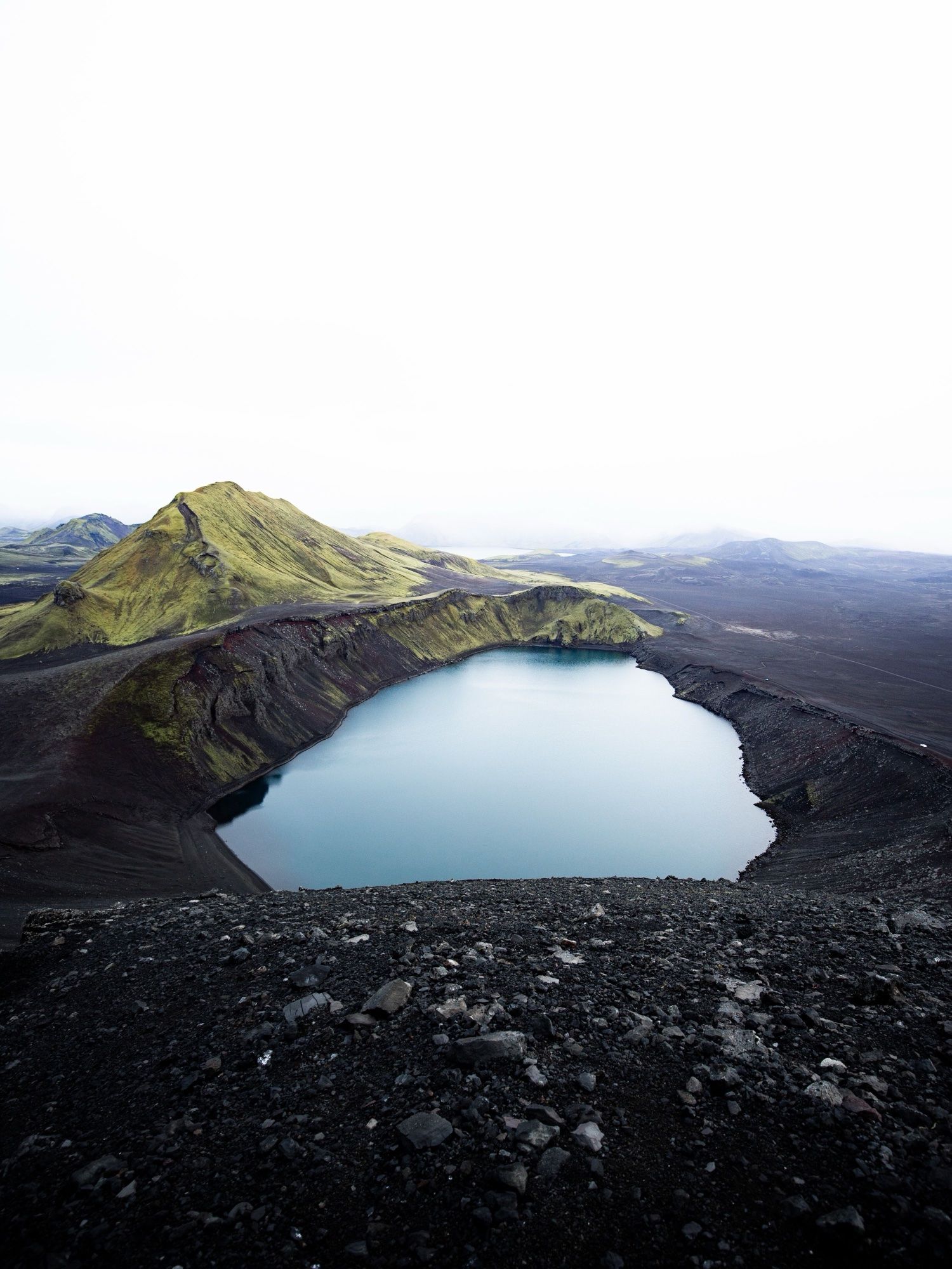 A blue crater lake beside a moss-green mountain in the highlands