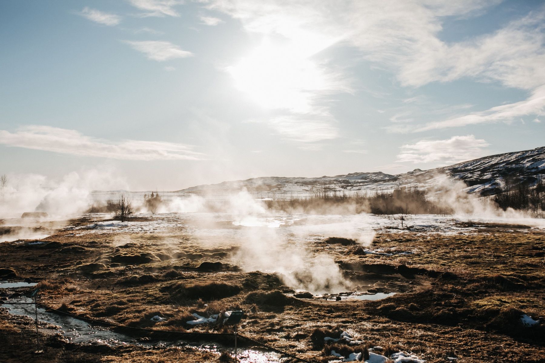 Steam rising from hot springs in the Geysir geothermal field on a sunny winter day
