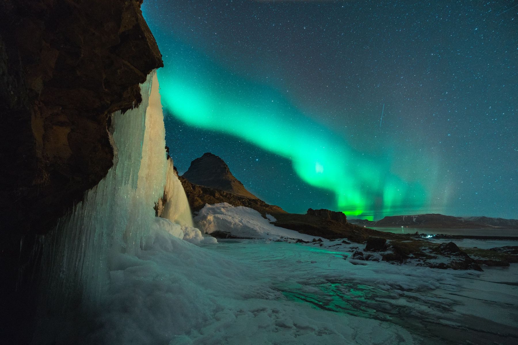 Northern lights over Kirkjufell mountain beside a frozen waterfall
