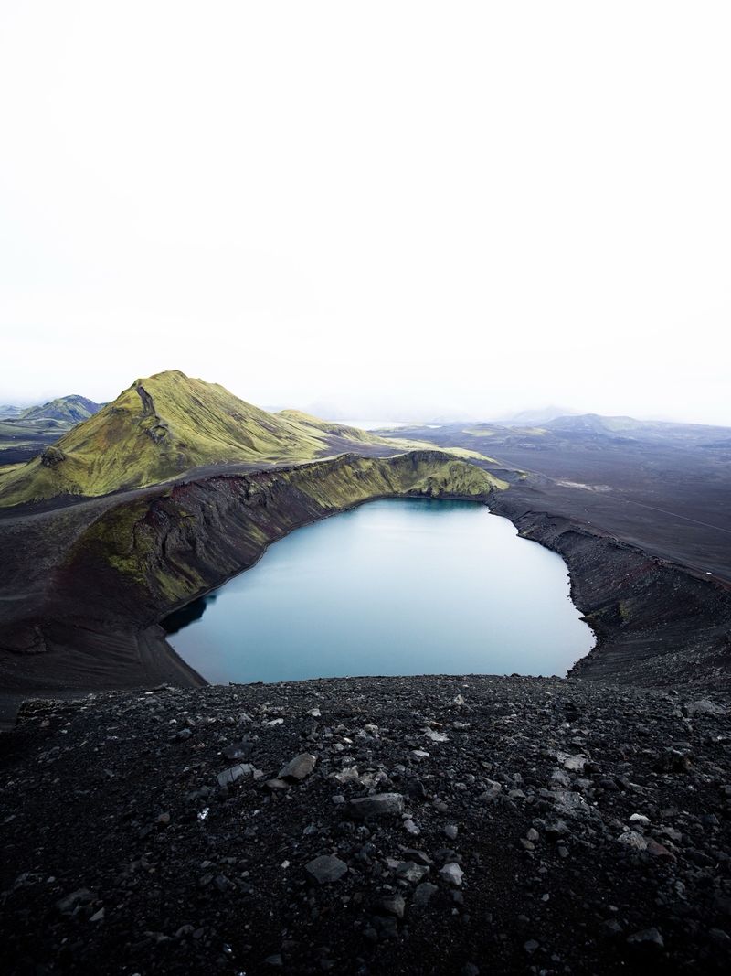 A blue crater lake beside a moss-green mountain