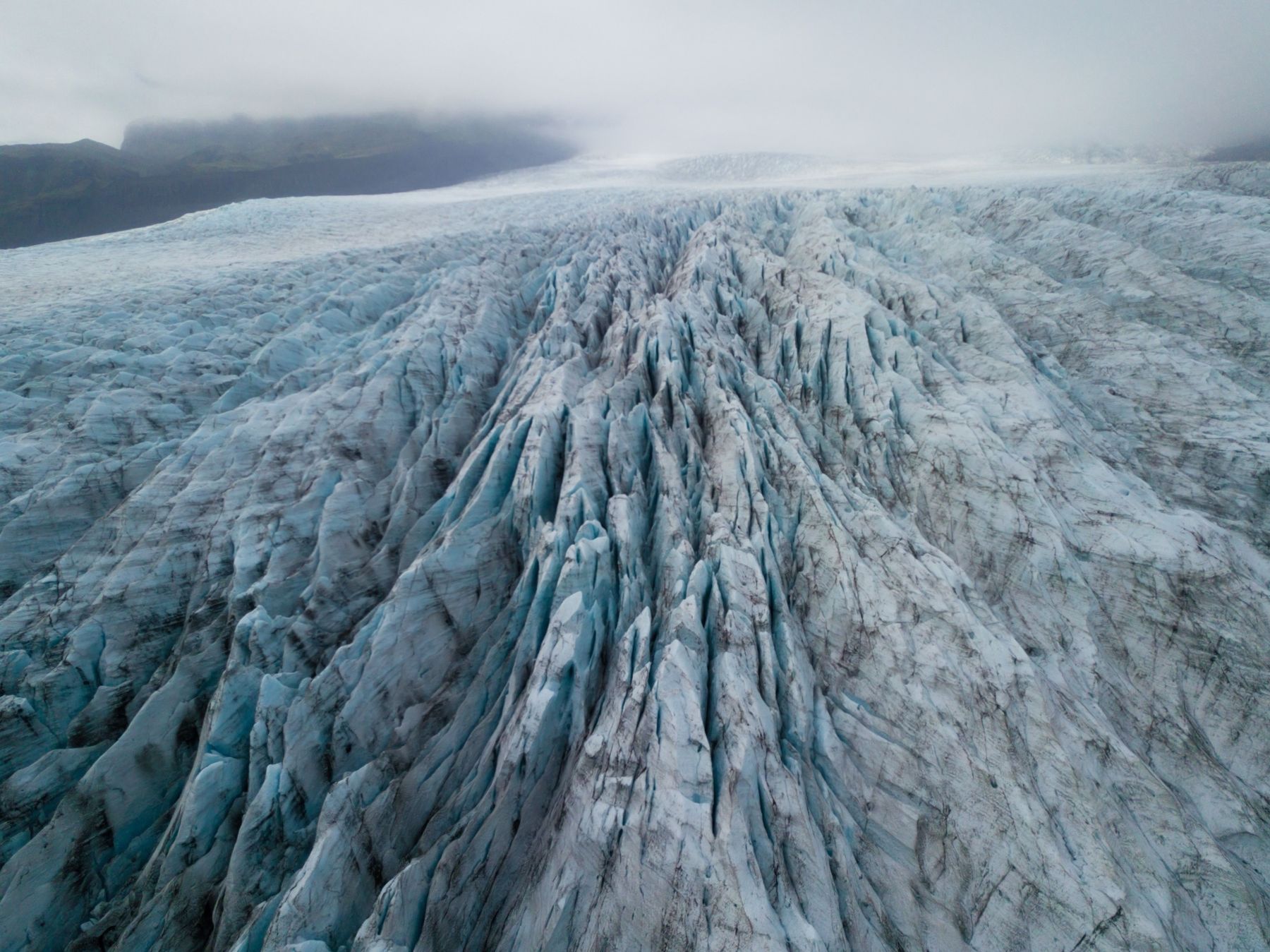 Deep blue crevasses running down a glacier, seen from above in mist