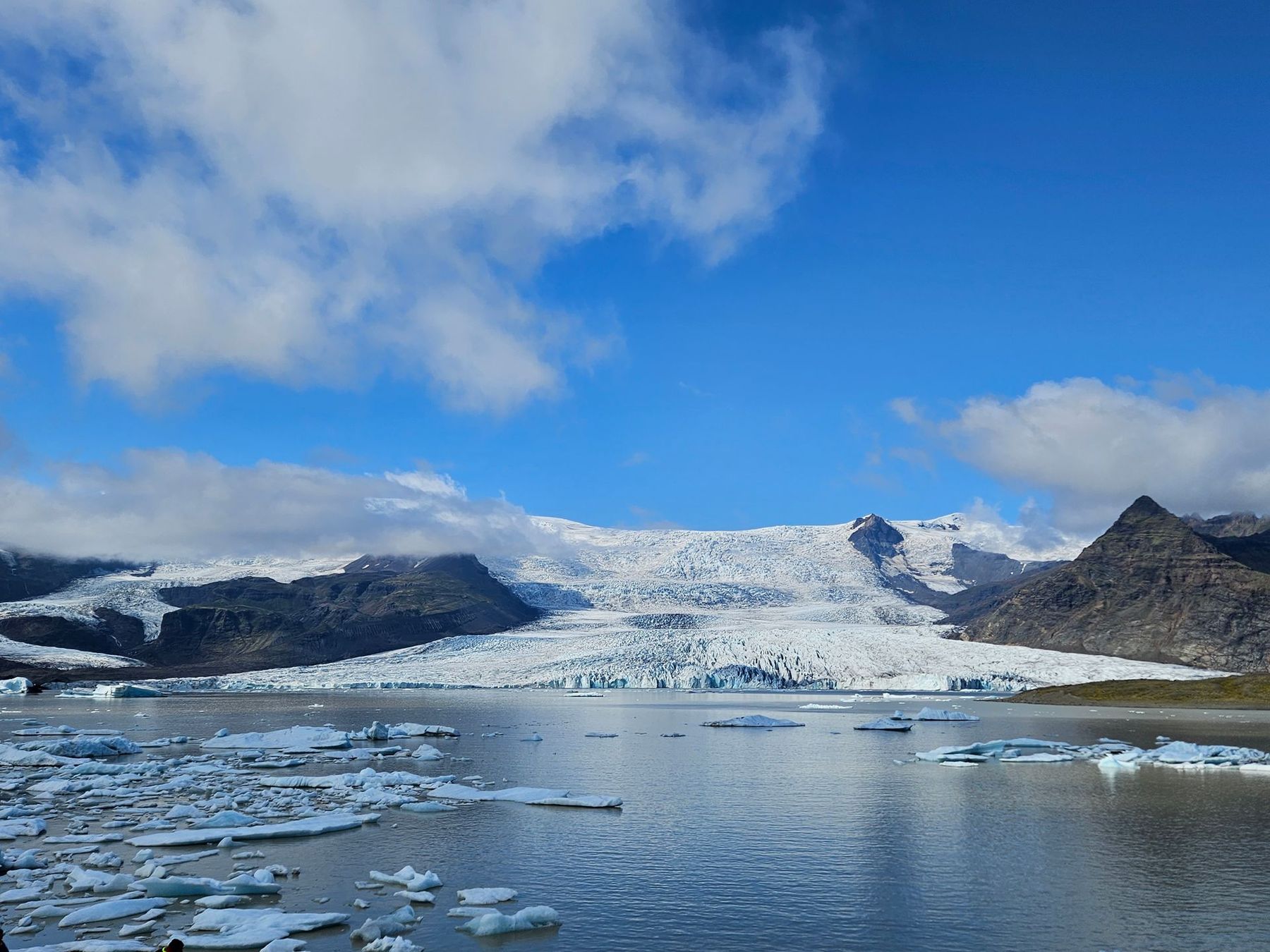 Fjallsárlón glacier lagoon with floating ice below a glacier and blue sky