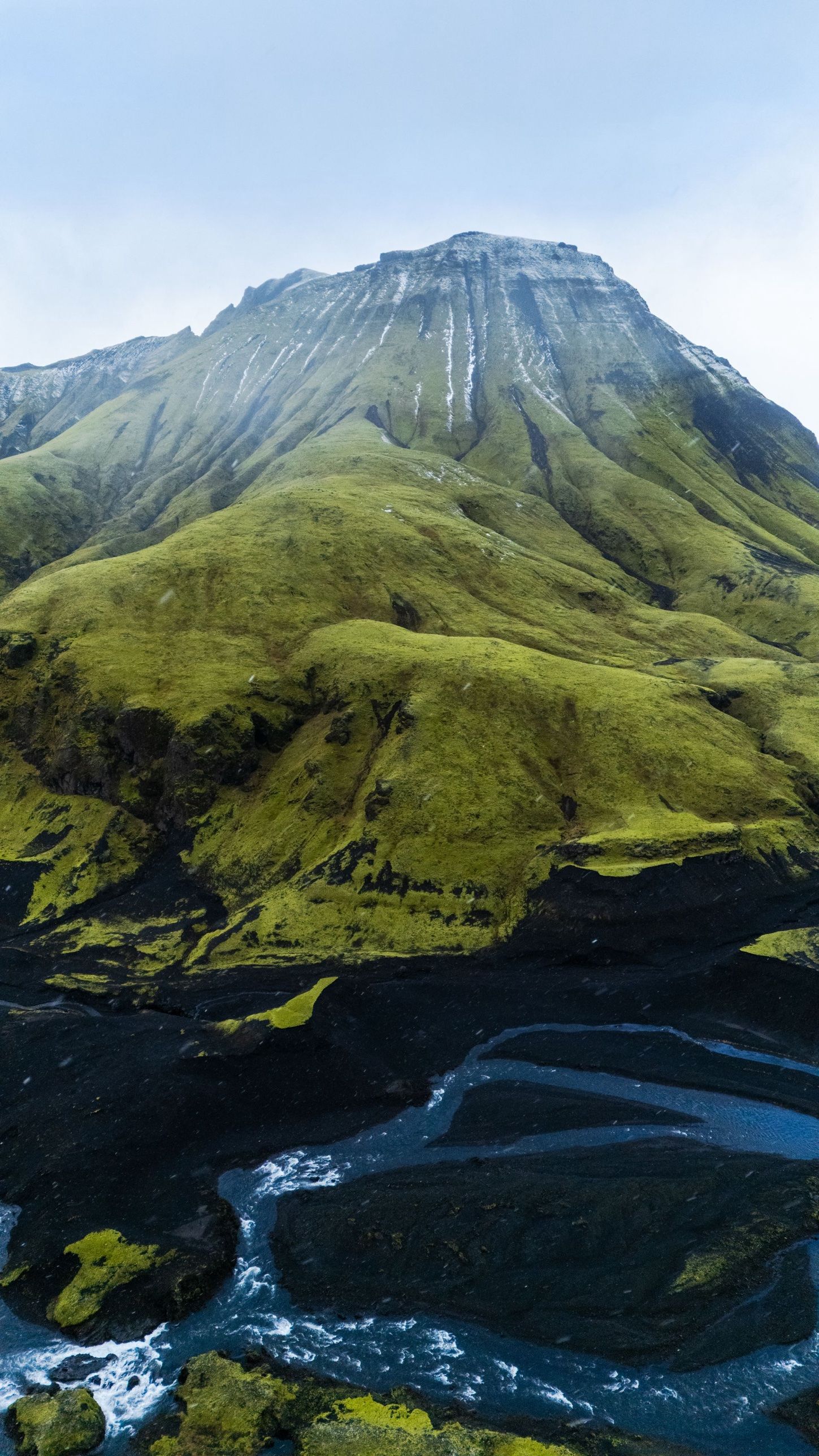 A moss-green mountain above a braided river and black sand in the Icelandic highlands