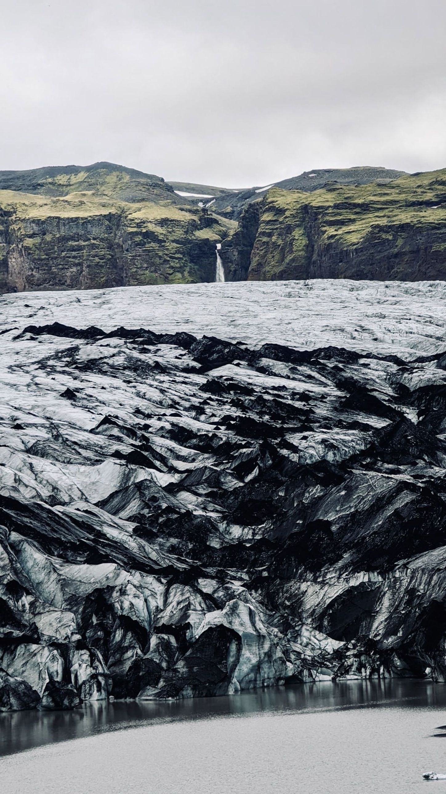 The ash-streaked ice of Sólheimajökull with a waterfall in the cliffs above