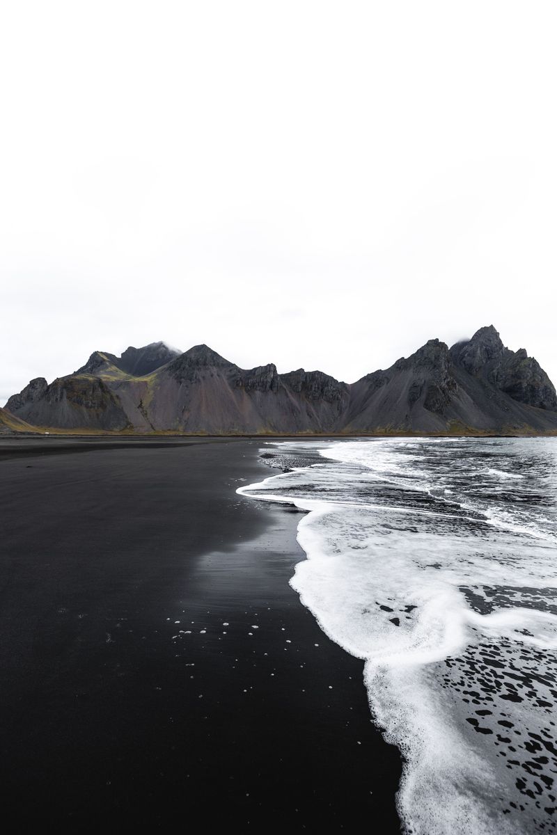 White surf running onto a black beach below a dark mountain range