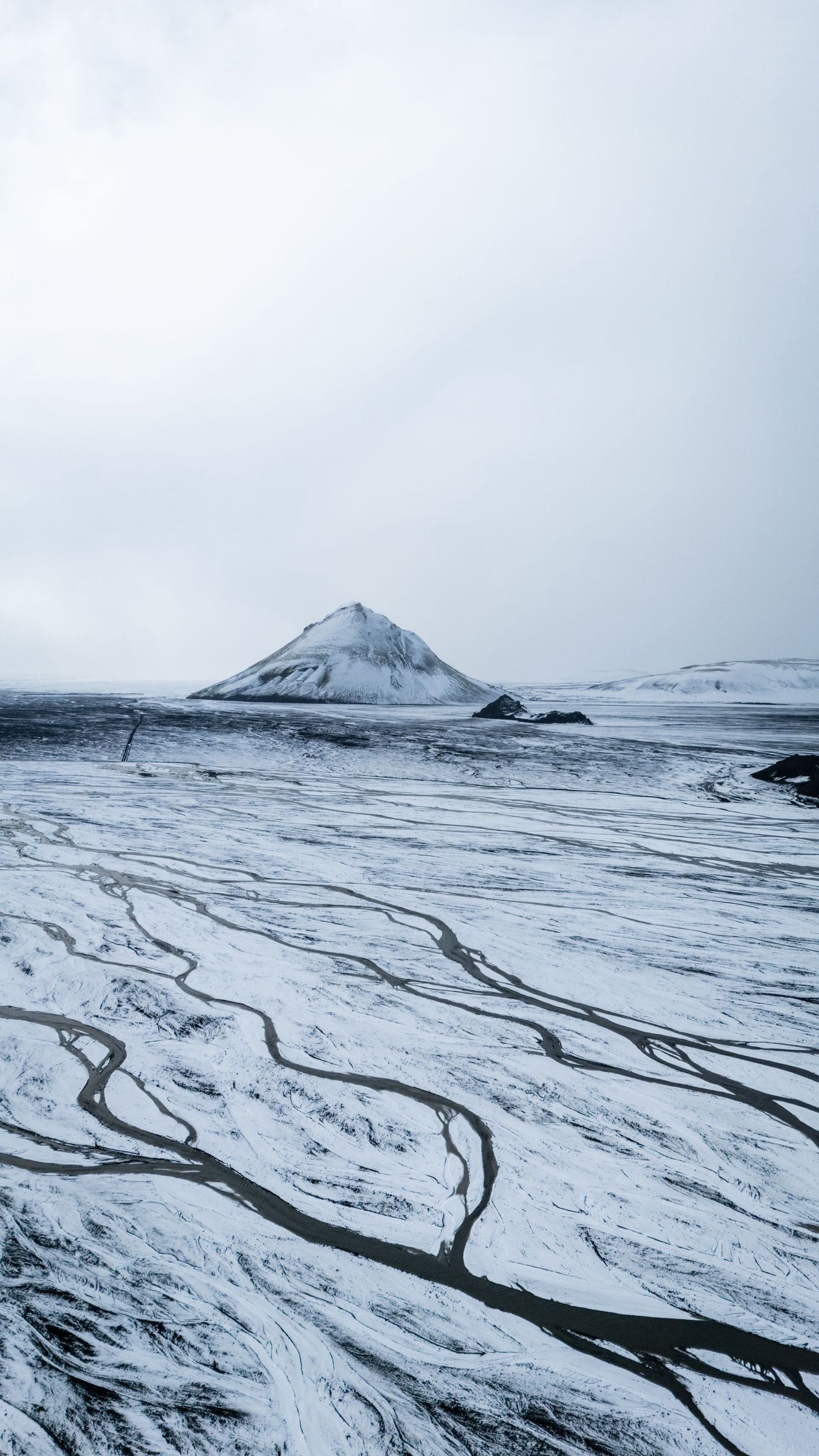 A lone snow-covered mountain above a white plain cut by dark meltwater channels
