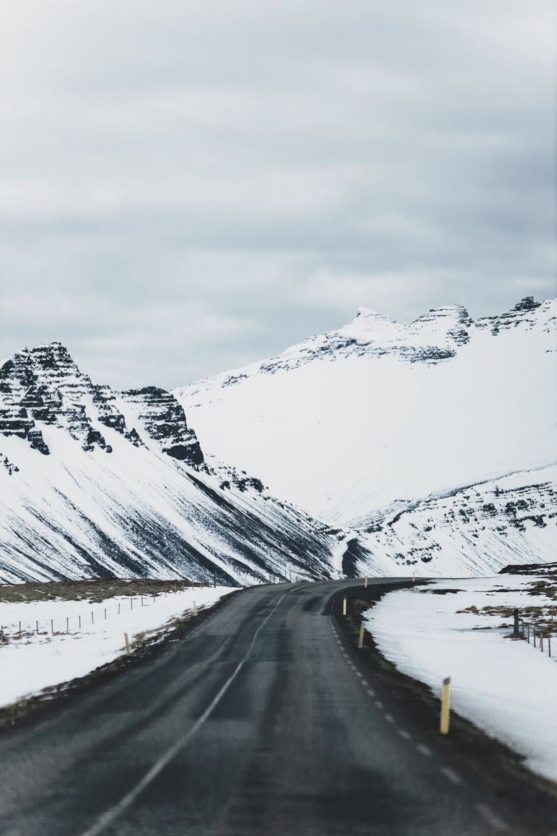 A cleared two-lane road winding between snow-covered mountains under a grey winter sky